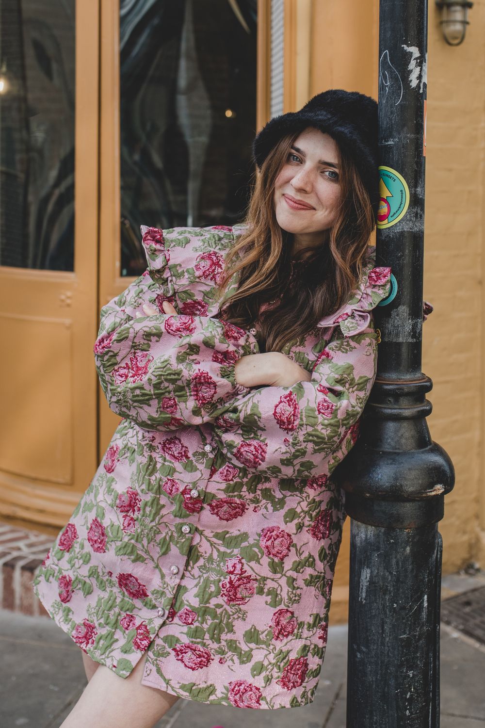 Casual pose in floral dress and black hat by vintage lamppost.