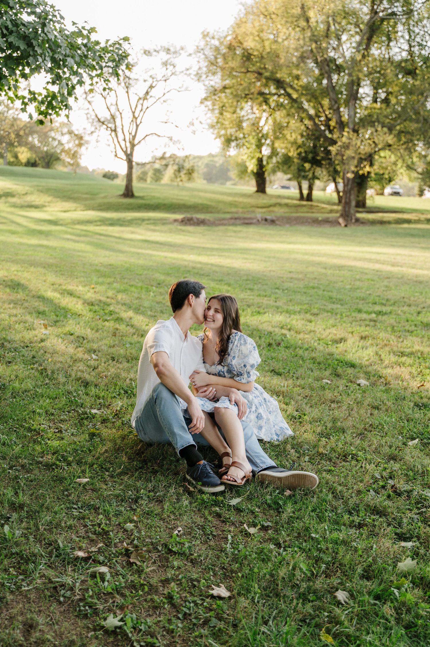 Couple sits side by side in green field as the sun sets behind them