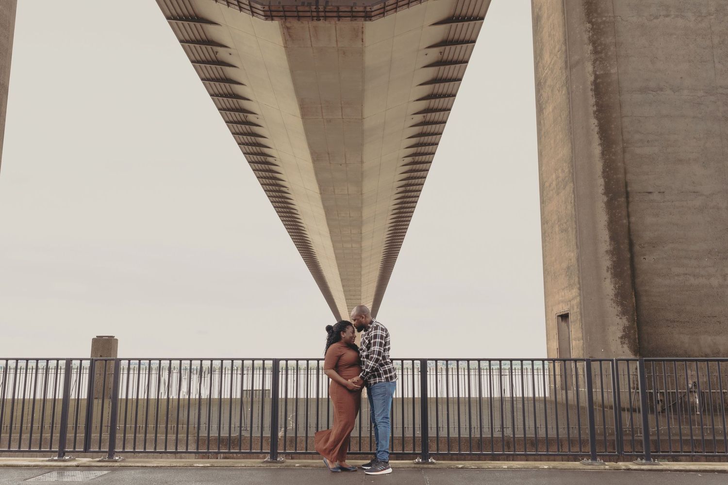 Couple standing beneath large concrete bridge supports during maternity session. Photographer. Hull. East Yorkshire. Photography
