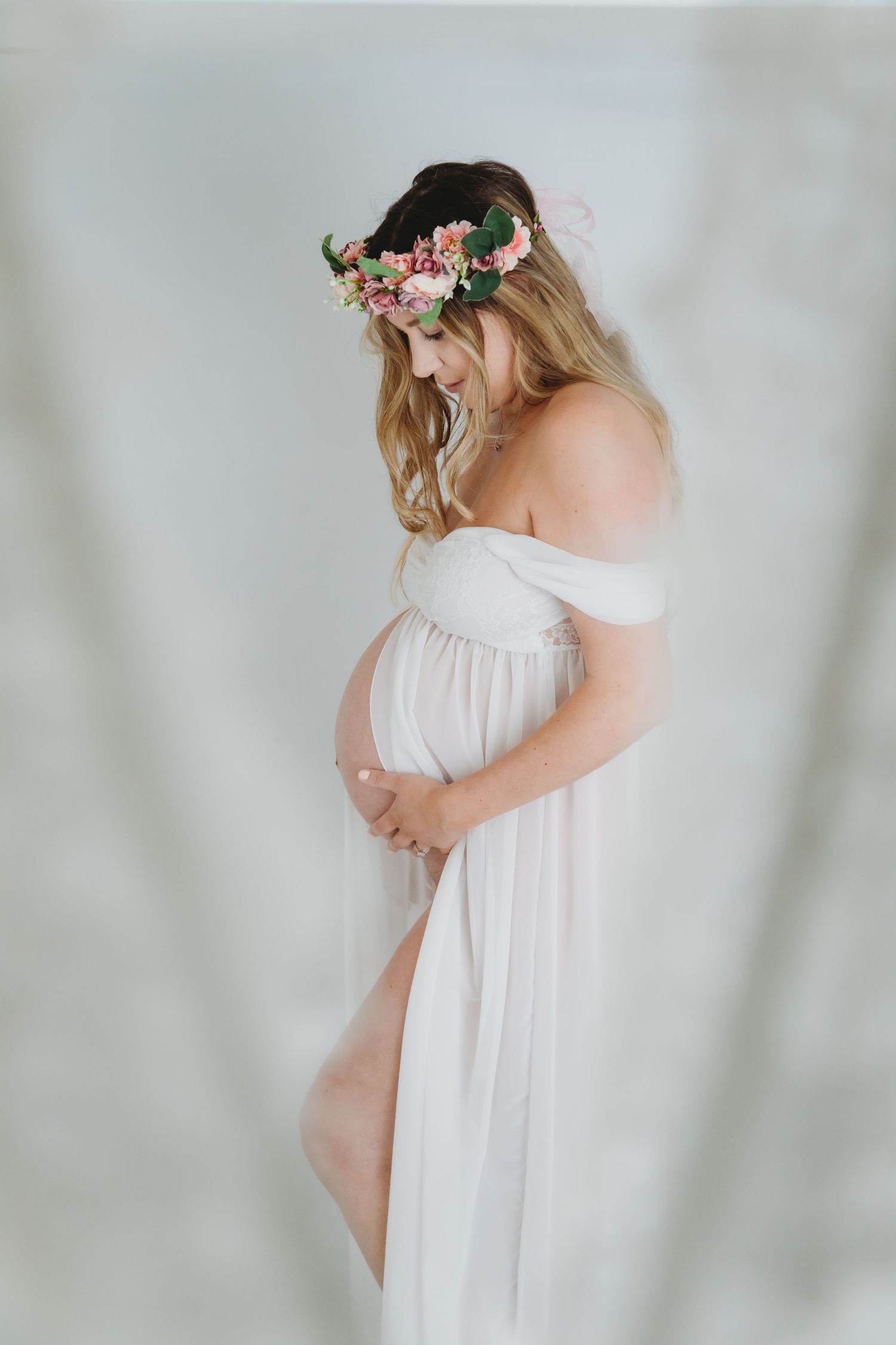 Maternity photos of woman in white dress with floral crown against light backdrop. Photographer. Hull. East Yorkshire. Photography