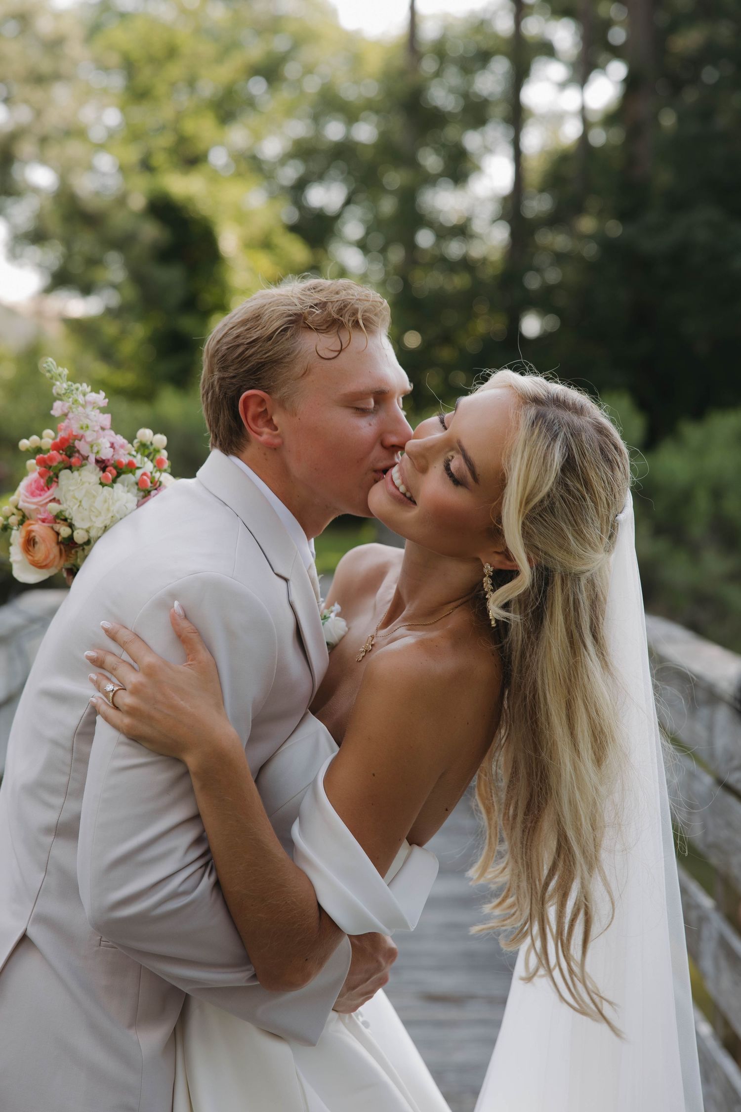 A wedding couple poses in a scenic mountain meadow with a beautiful floral bouquet.