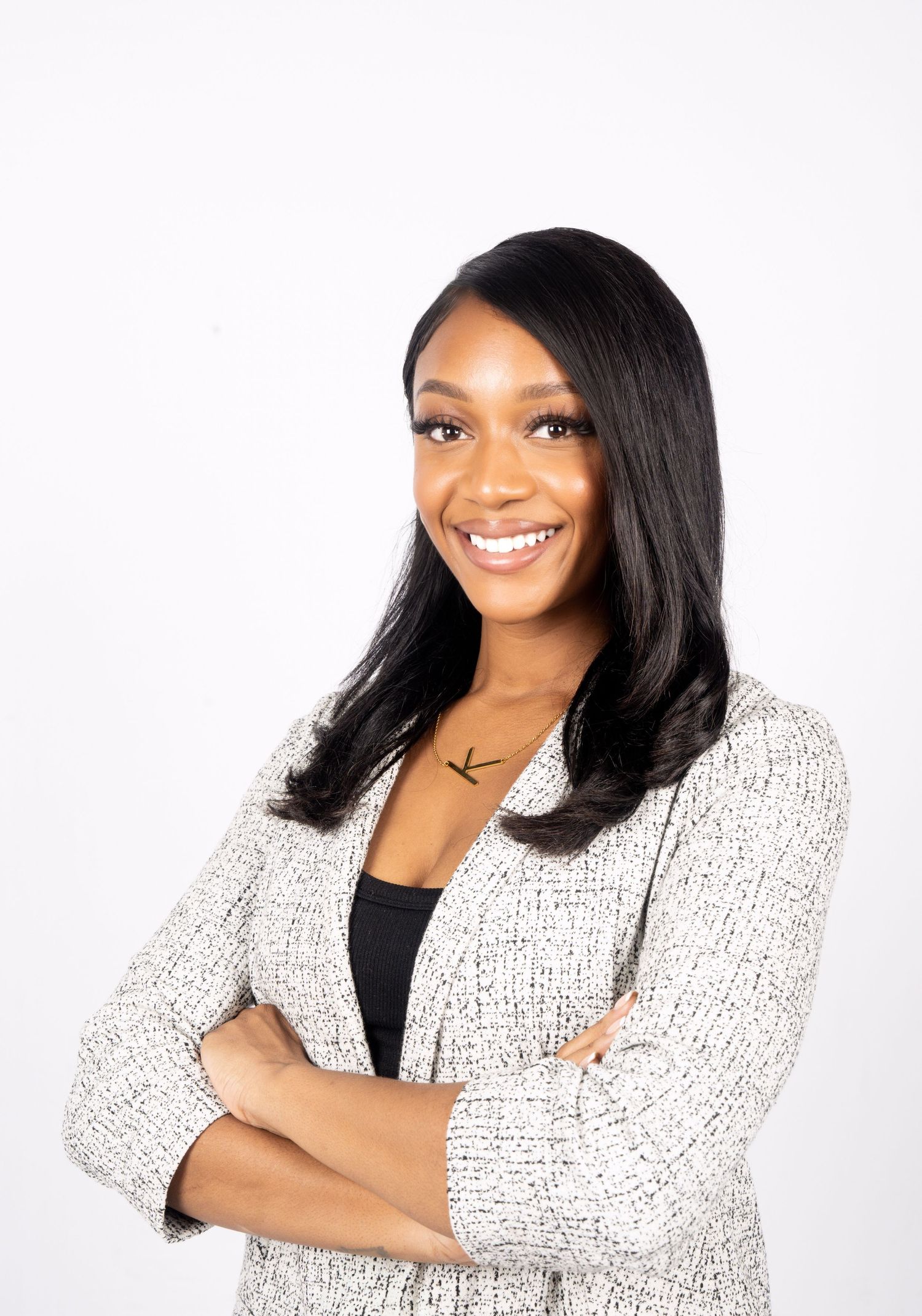 Professional portrait of someone wearing a black top and textured white blazer posing with crossed arms against white background.