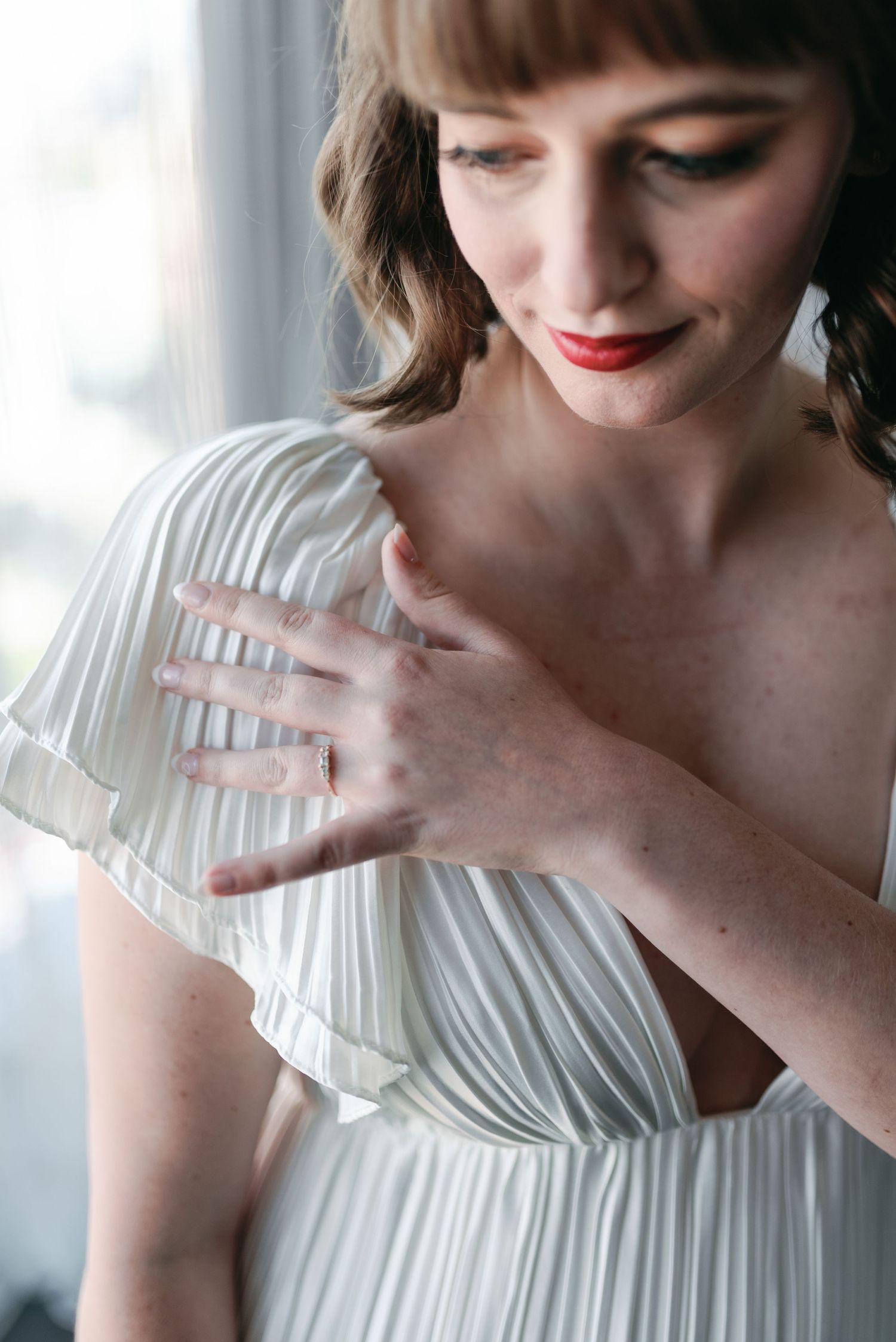 A delicate white pleated dress detail with hands gracefully touching the fabric.