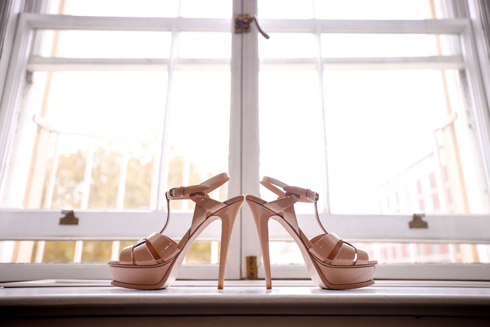 Elegant white bridal heels displayed on a bright windowsill, creating a romantic wedding day detail shot. Asian Wedding Photography & Videog