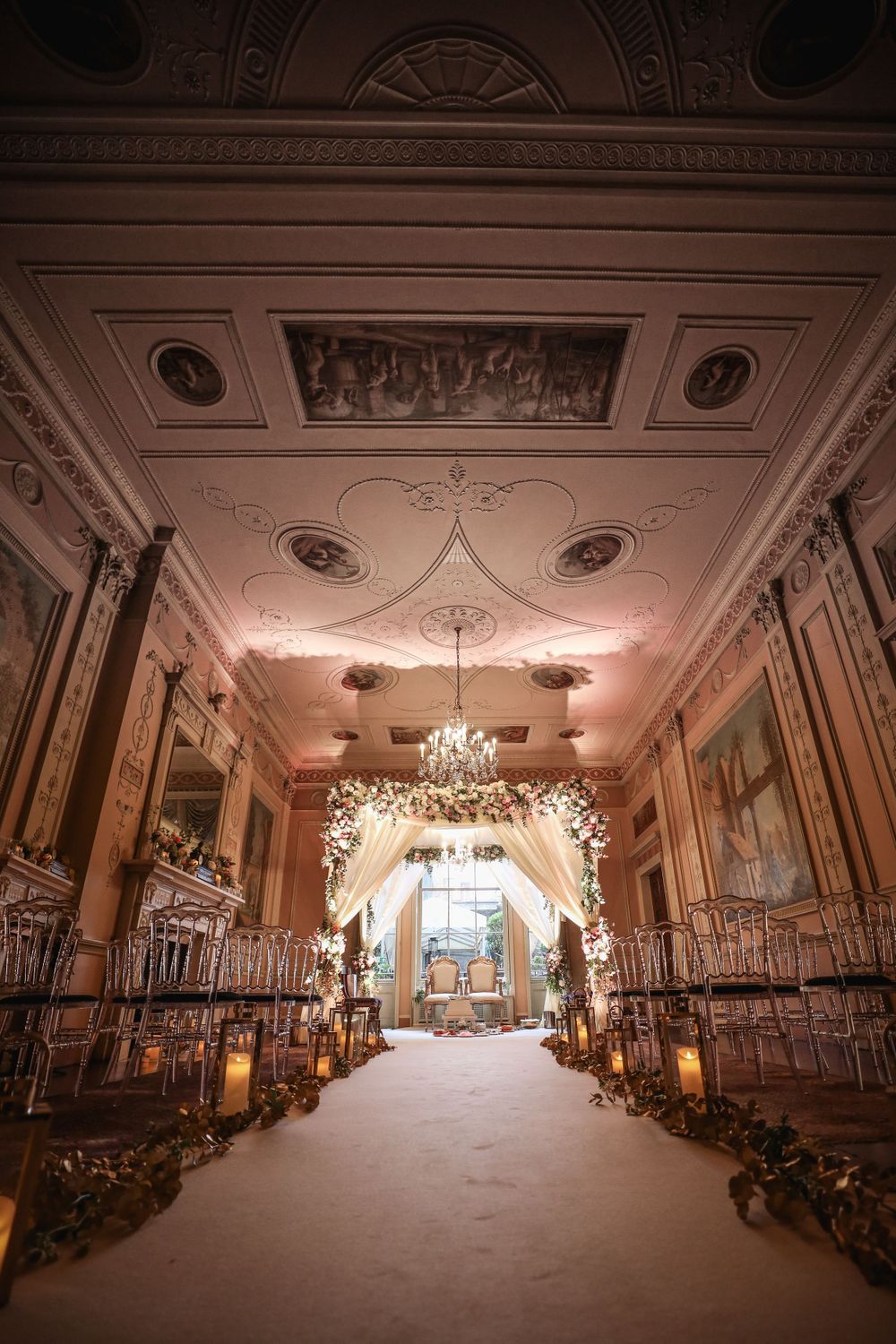 An ornate wedding ceremony aisle with crystal chandeliers and floral arch in a luxurious ballroom. Asian Wedding Photography & Videography