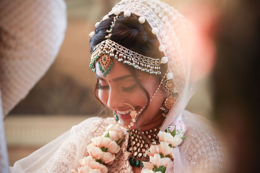 Traditional Indian bride wearing an ornate white wedding dress with detailed headpiece and jewelry smiles during ceremony. Asian Weddings