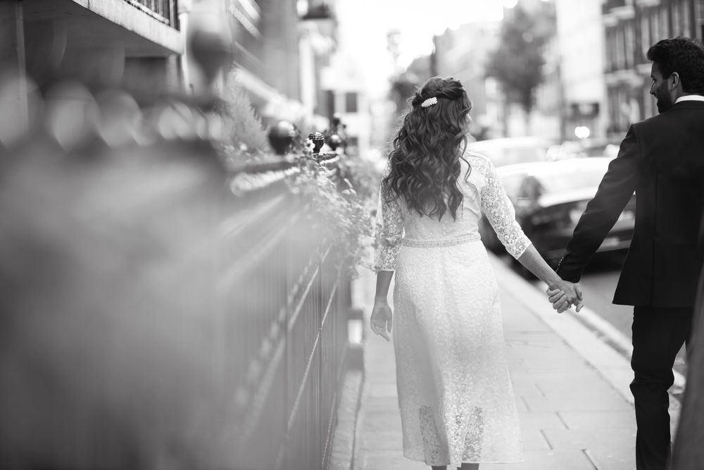 Black and white shot of couple walking hand in hand down urban street after wedding. Hindu Wedding Photography