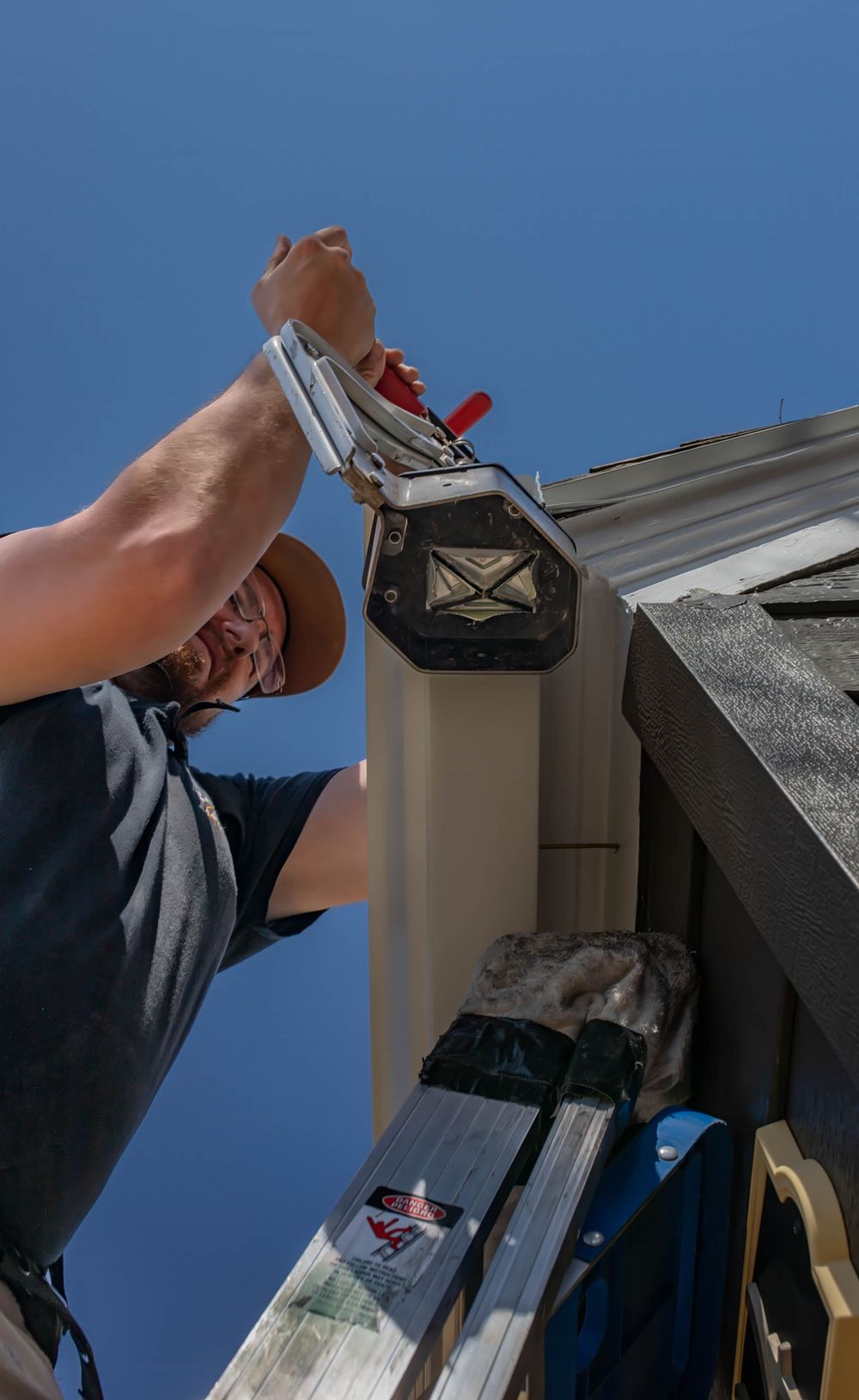 Professional handyman works on installing a gutter system on a residential home against blue sky background.