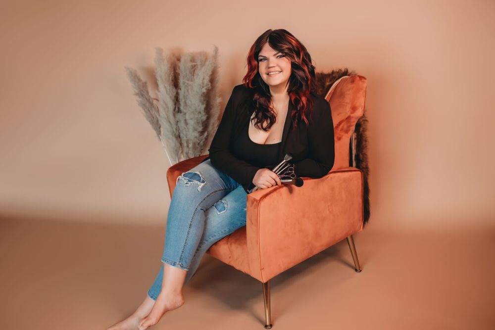 A woman relaxes in an orange velvet armchair wearing a black blazer and ripped jeans.