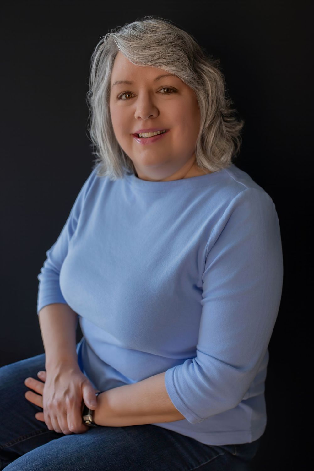 Person with silver hair wearing a light blue top poses against dark background in artistic portrait series.