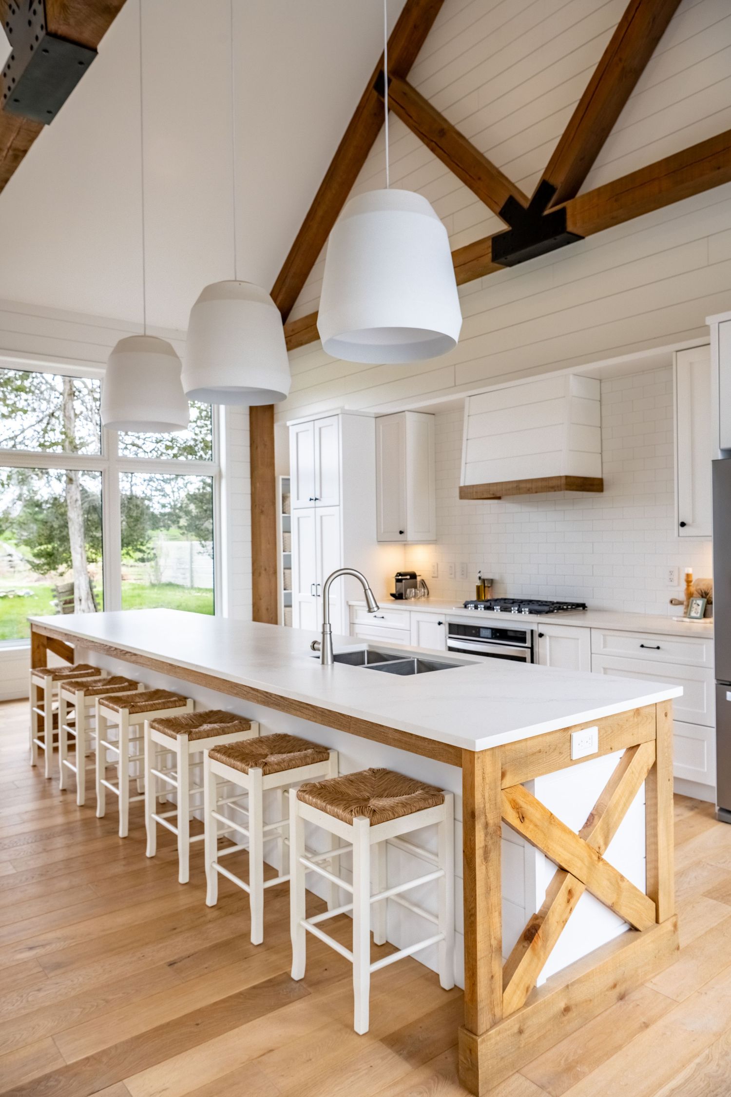 Modern white kitchen with vaulted ceiling, exposed wooden beams, and a large central island with bar seating.