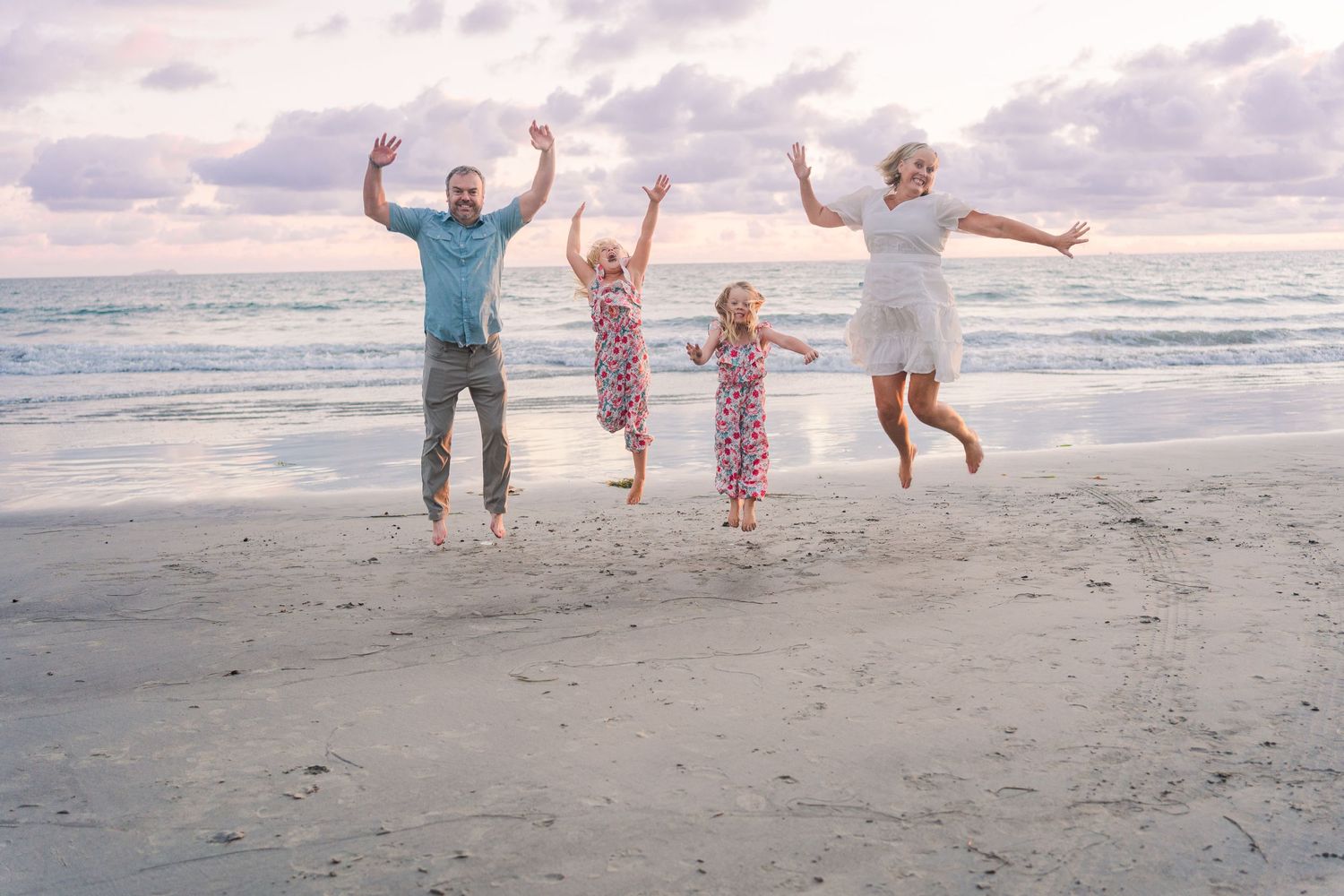 Group jumping with joy on beach at sunset against cloudy ocean backdrop.