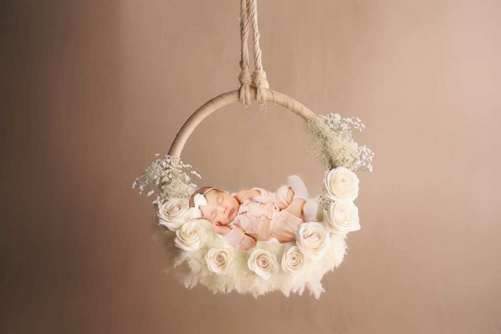 A delicate floral wreath with ivory and blush roses hangs on twine against a neutral beige backdrop.