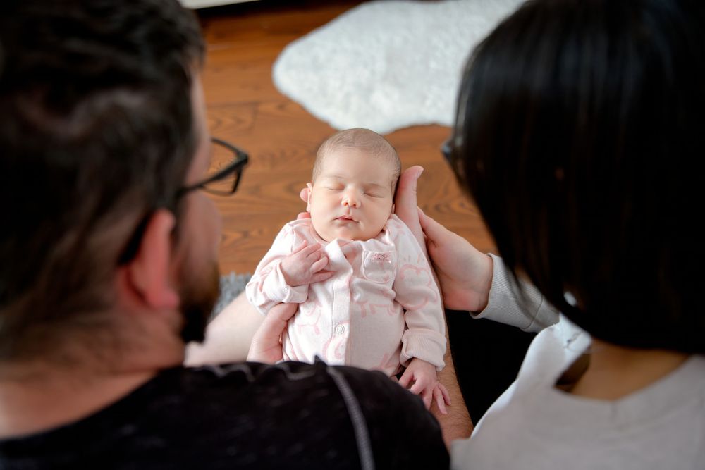 Baby in pink clothing appears content while being held by caregivers indoors.