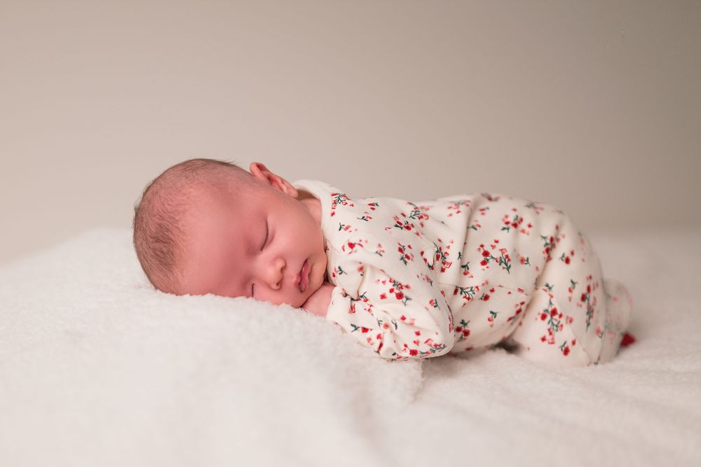 Newborn baby sleeping peacefully on white blanket wearing floral print onesie.