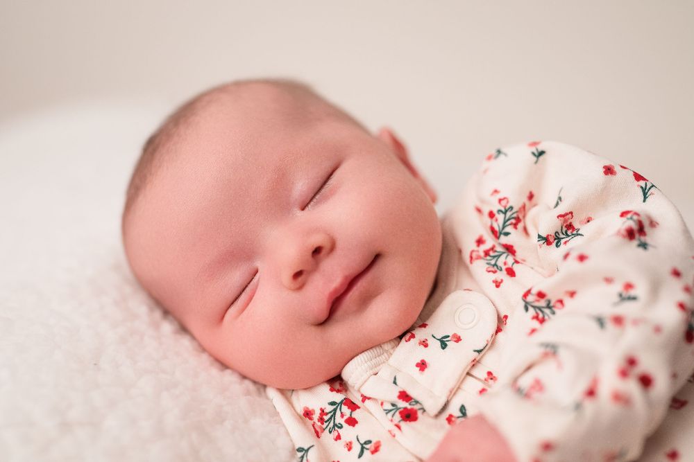 Sleeping infant in white and red floral outfit against neutral backdrop.