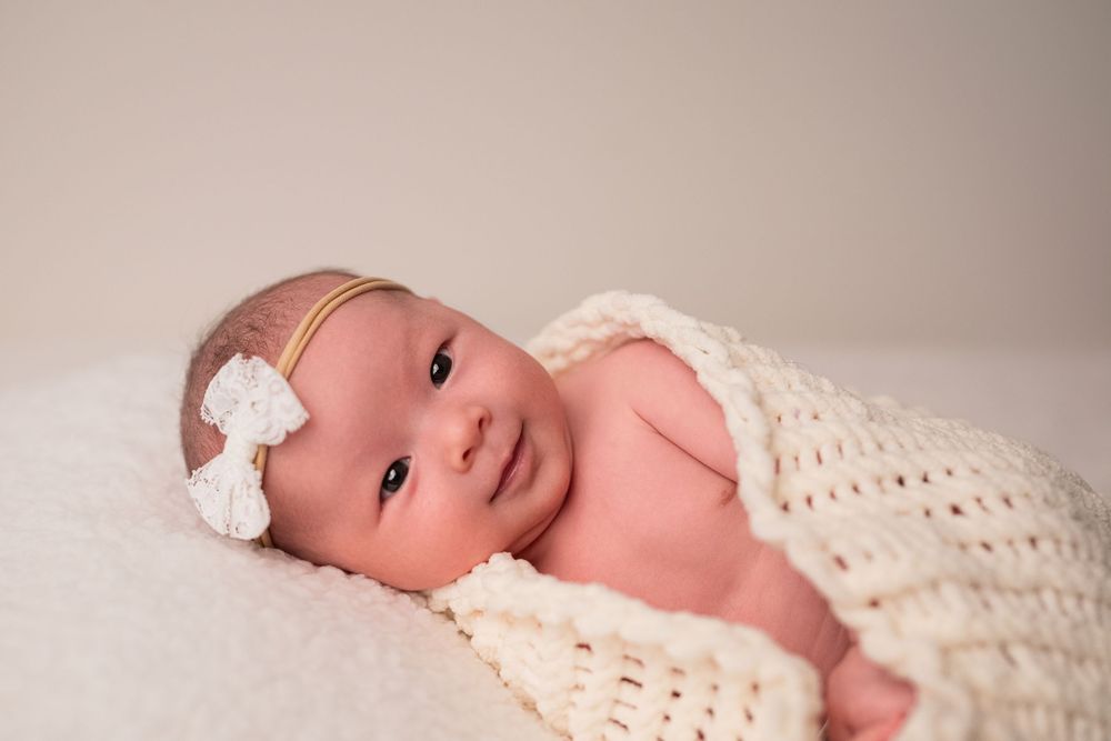 Baby lying on cream blanket wearing white knit wrap with eyes open.