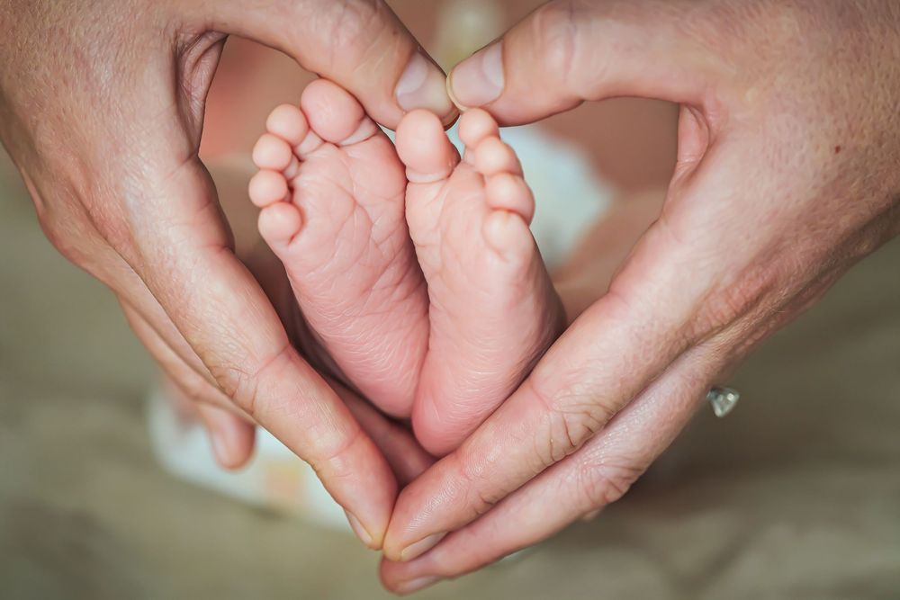 Close-up photo of tiny baby feet being gently held by adult hands in soft natural lighting.