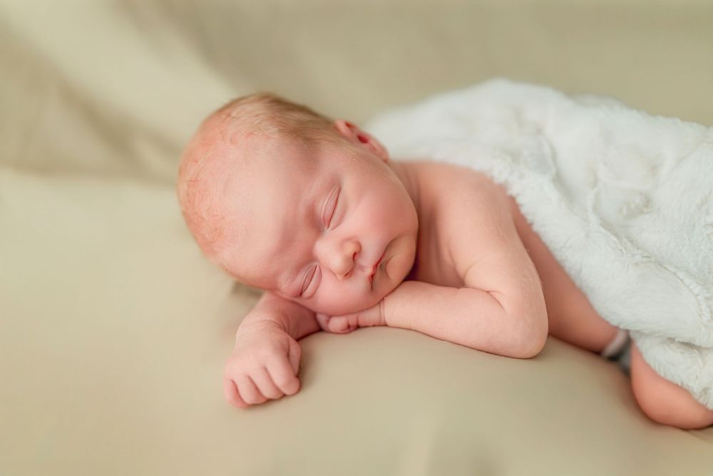 Peaceful sleeping newborn baby wrapped in soft white blankets on a neutral background.