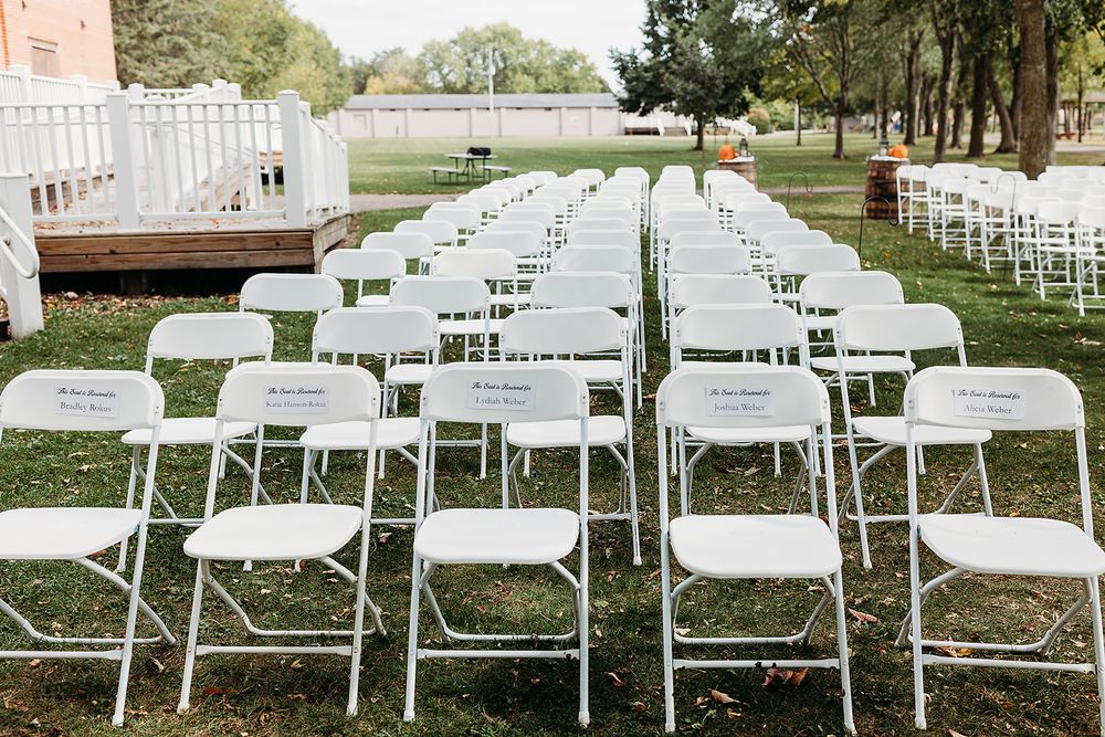 Rows of white folding chairs set up on grass for an outdoor ceremony with trees in the background.
