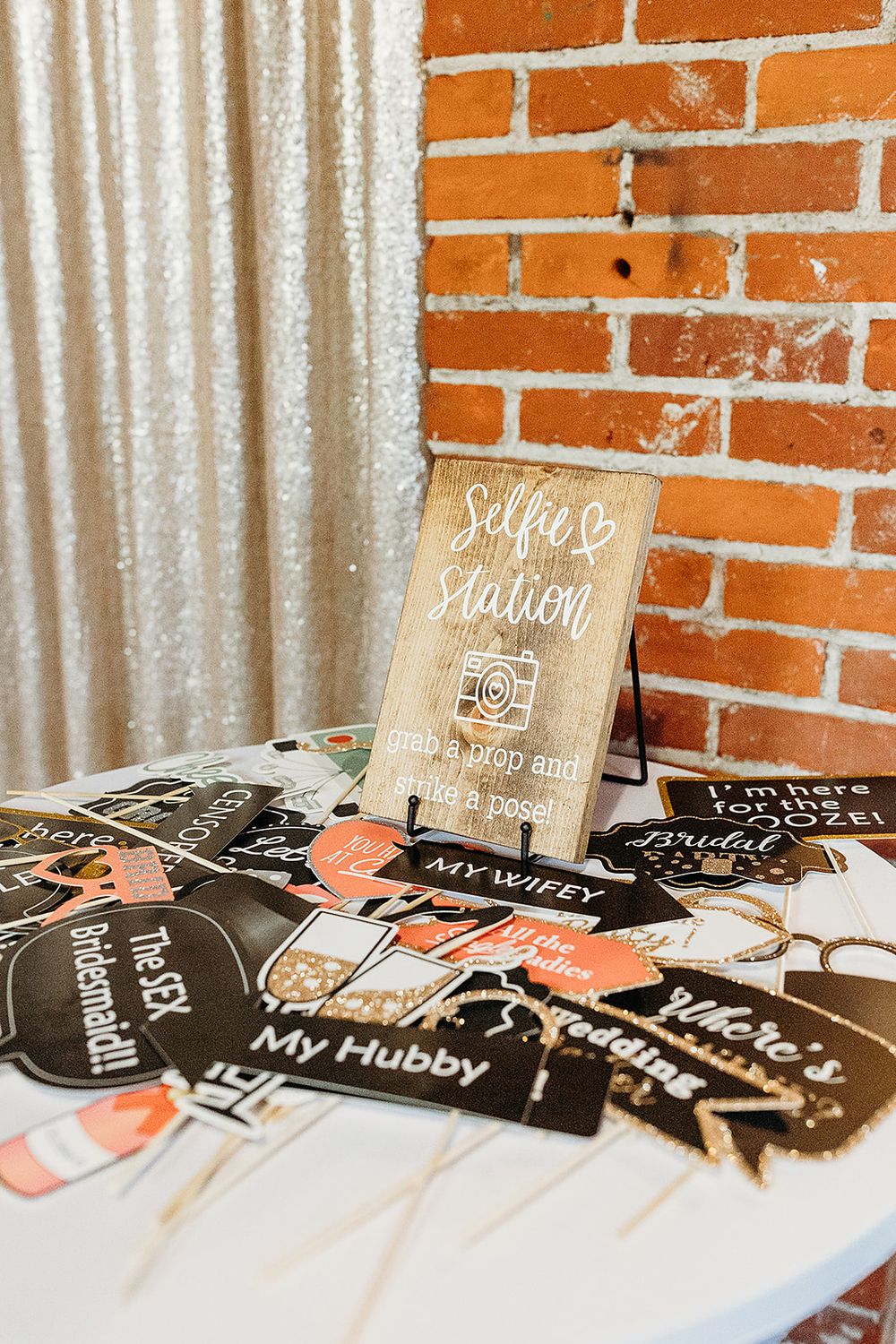 Wedding decorations display with custom photo props and wooden signage against a brick wall and white curtain backdrop.