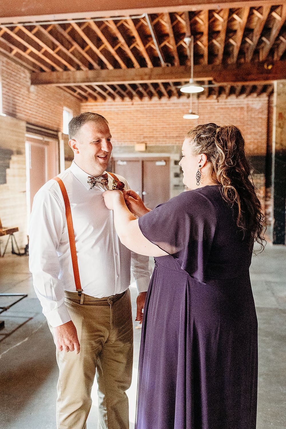 A wedding preparation moment captured in a rustic brick venue with exposed wooden beams and natural lighting.