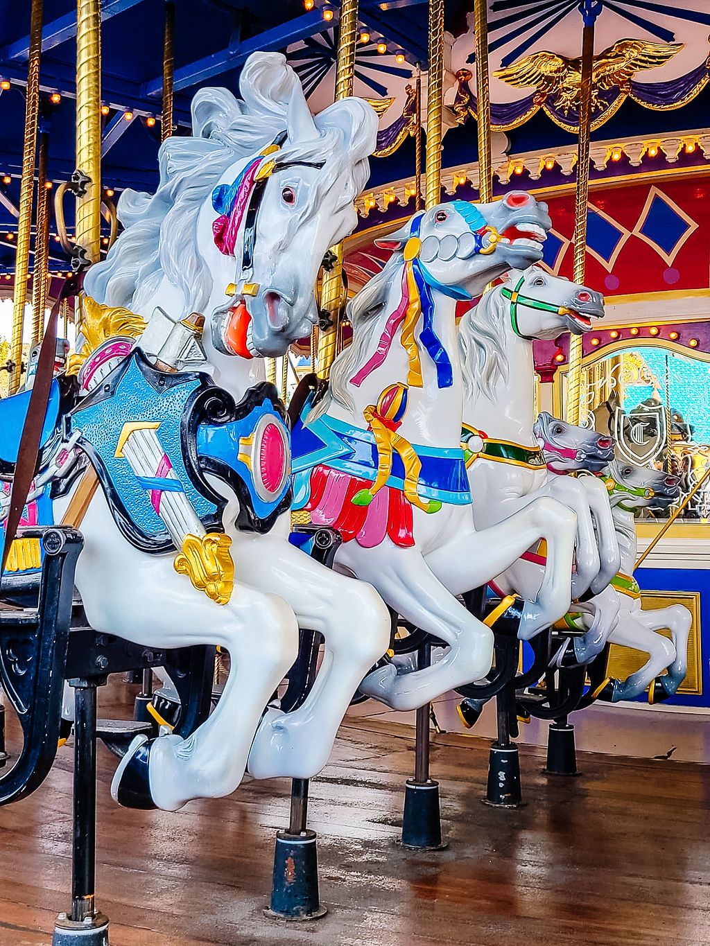 Colorful vintage carousel horses with white bodies and ornate decorations on a merry-go-round at an amusement park.