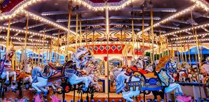 Illuminated carousel with colorful horses lit by festive string lights creates a magical carnival atmosphere at night.