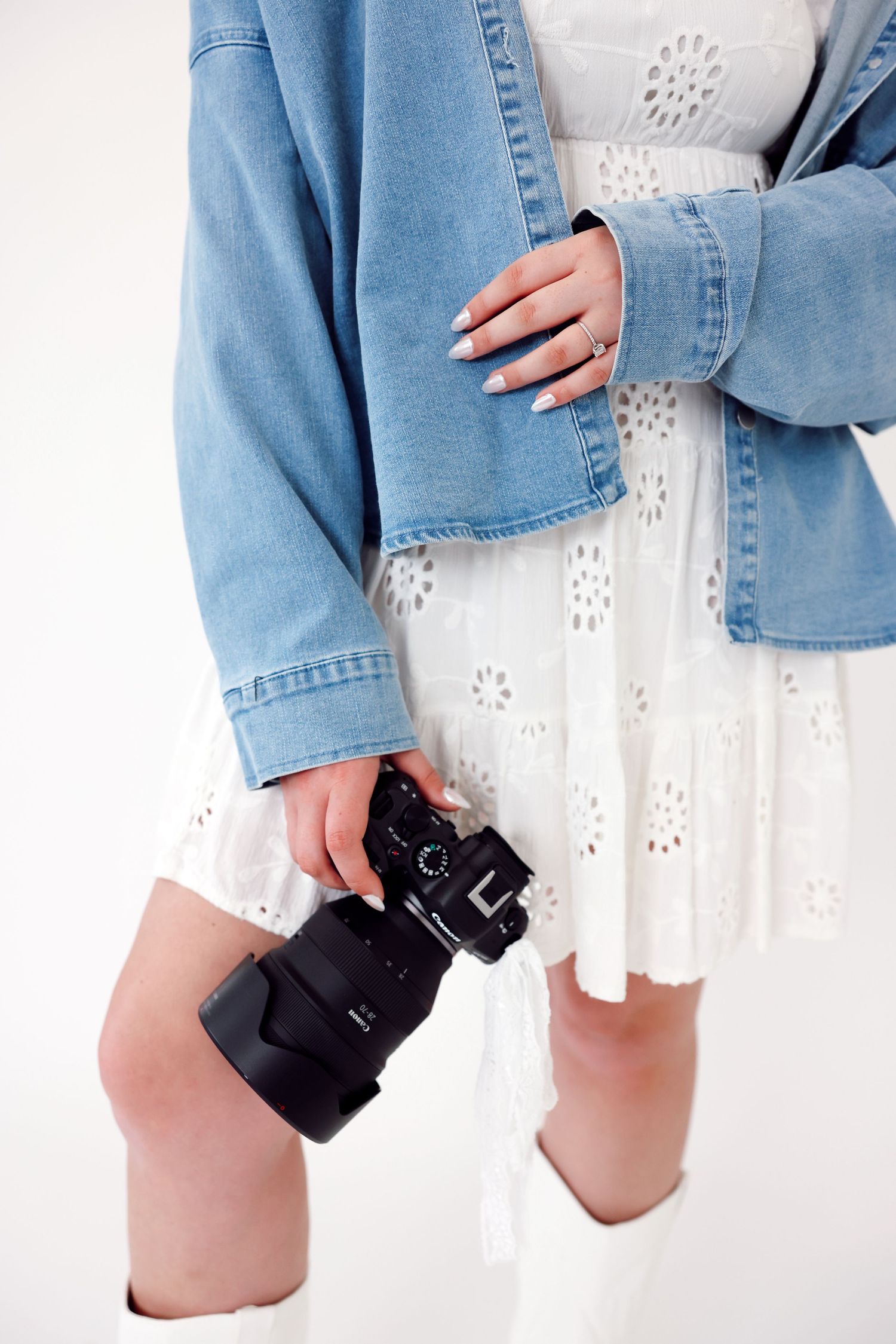 A person in denim overalls and white sweater laughs joyfully against a white backdrop while running hands through their hair.