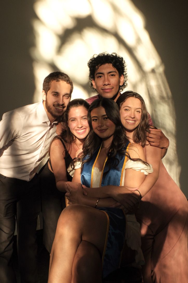A group of friends pose together at a party with dramatic lighting creating arch-like shadows on the wall behind them.
