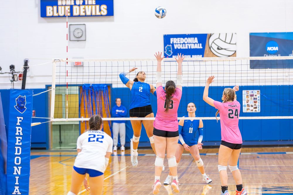 High school volleyball players practicing drills and skills in a blue and white gymnasium during team practice session.