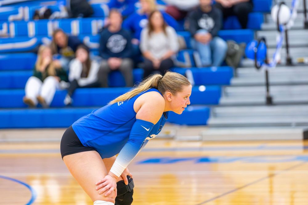 Volleyball player diving to save the ball during an intense match on a blue court.
