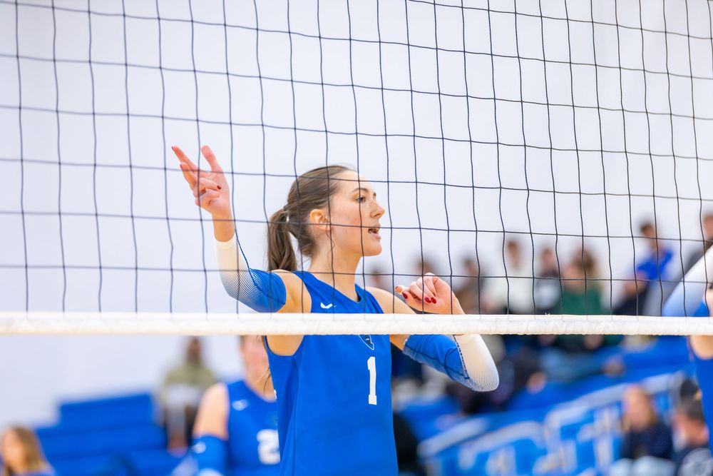 Two volleyball players at the net jump up to block a spike during an intense match.