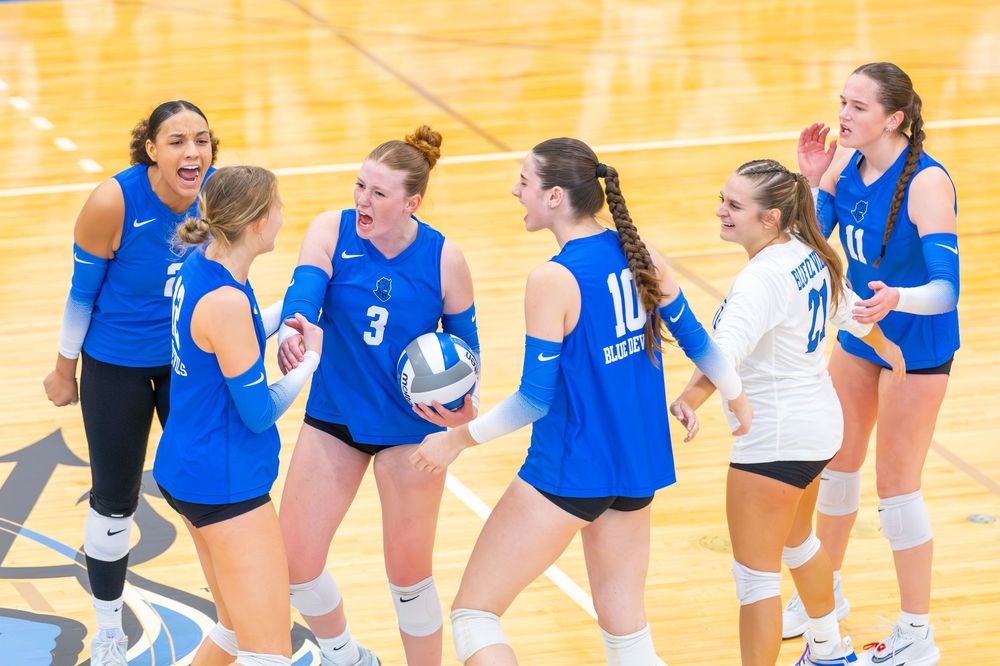 Volleyball players in blue uniforms celebrate together on the court after scoring a point.