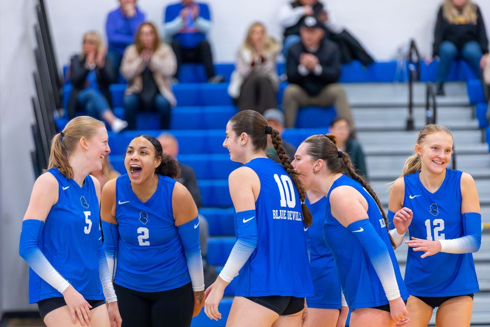 A volleyball team celebrates together on the court after scoring a point during a competitive match.