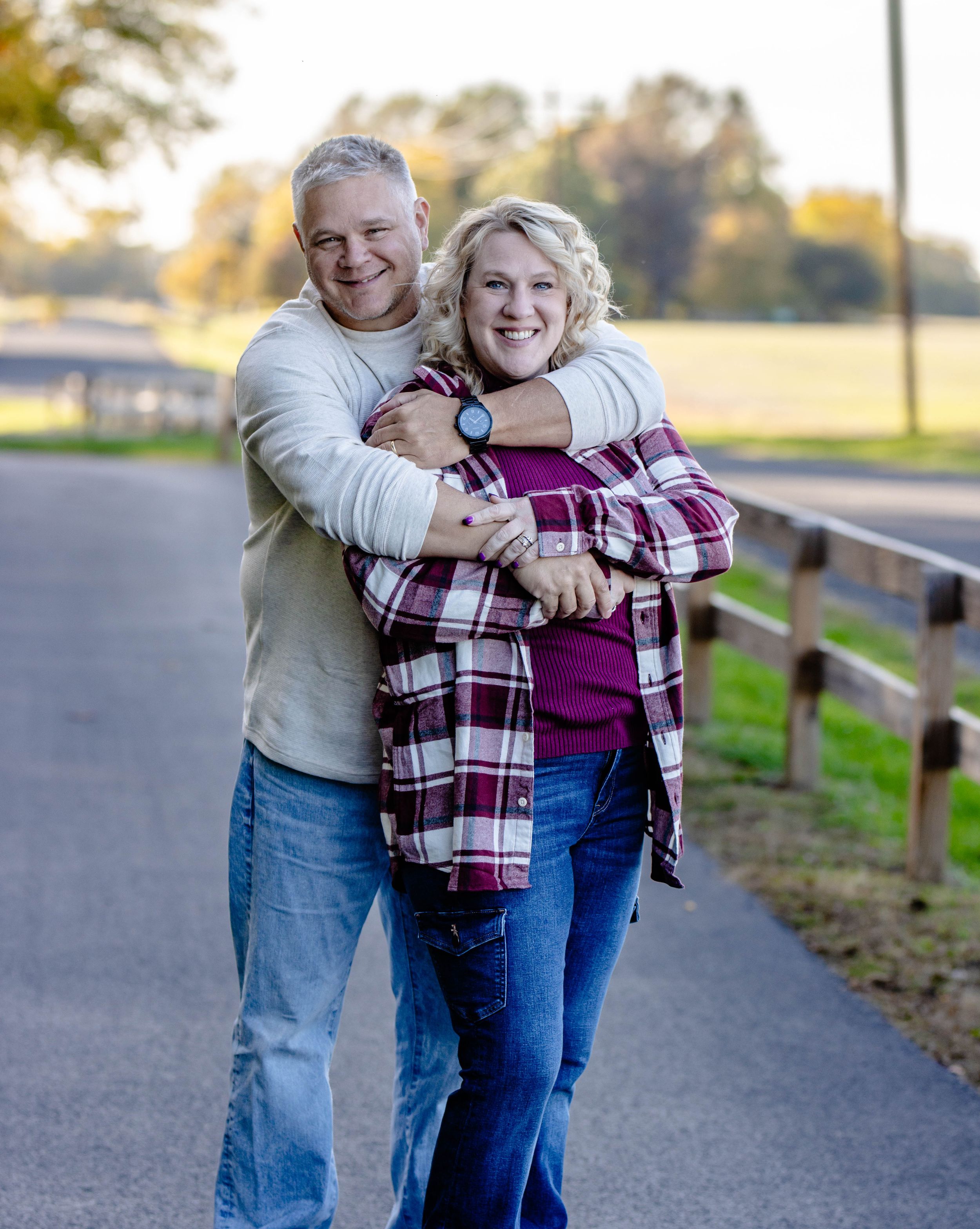 Couple embracing on walking path during autumn with colorful foliage in background.