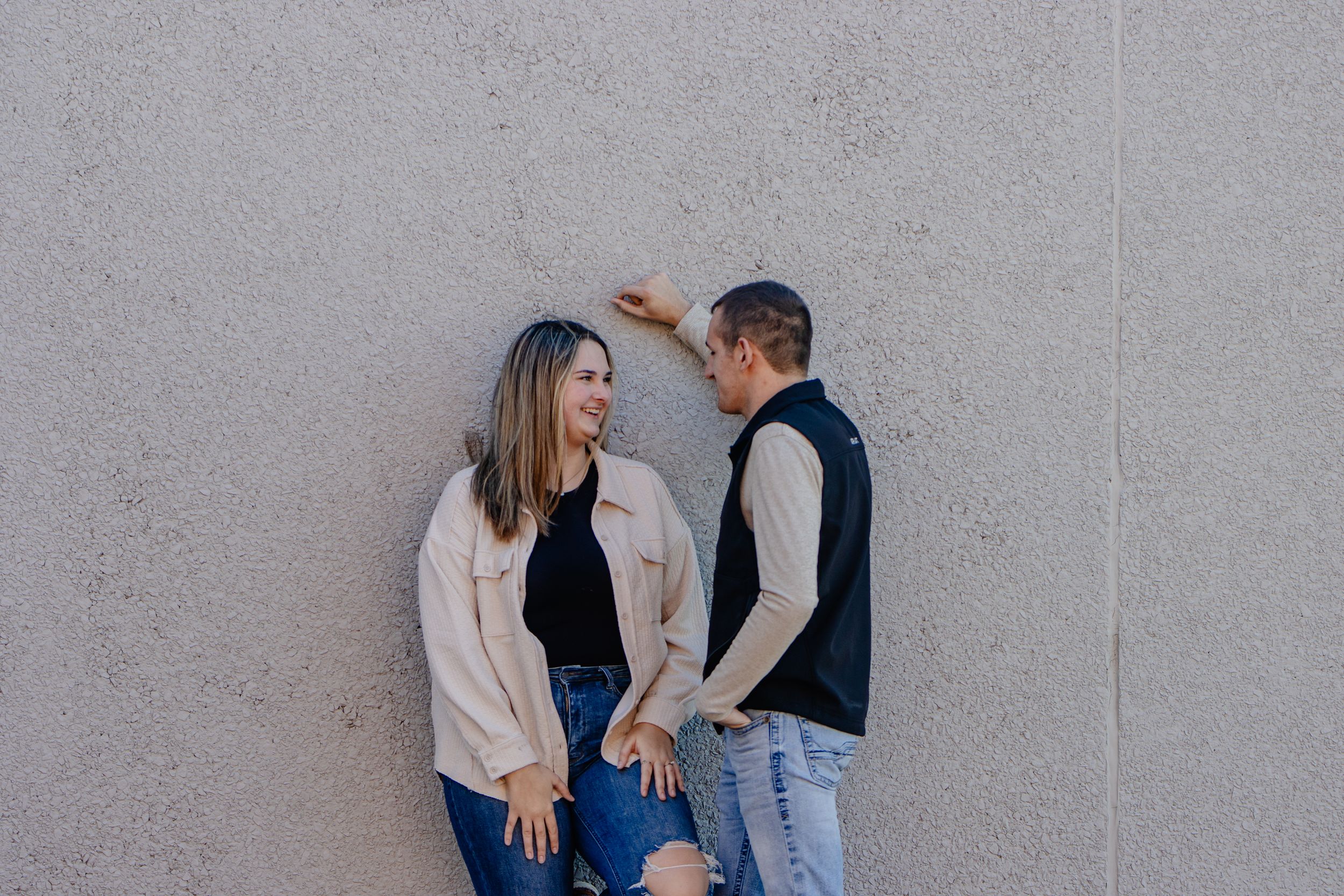 A couple shares a playful moment against a grey wall background.