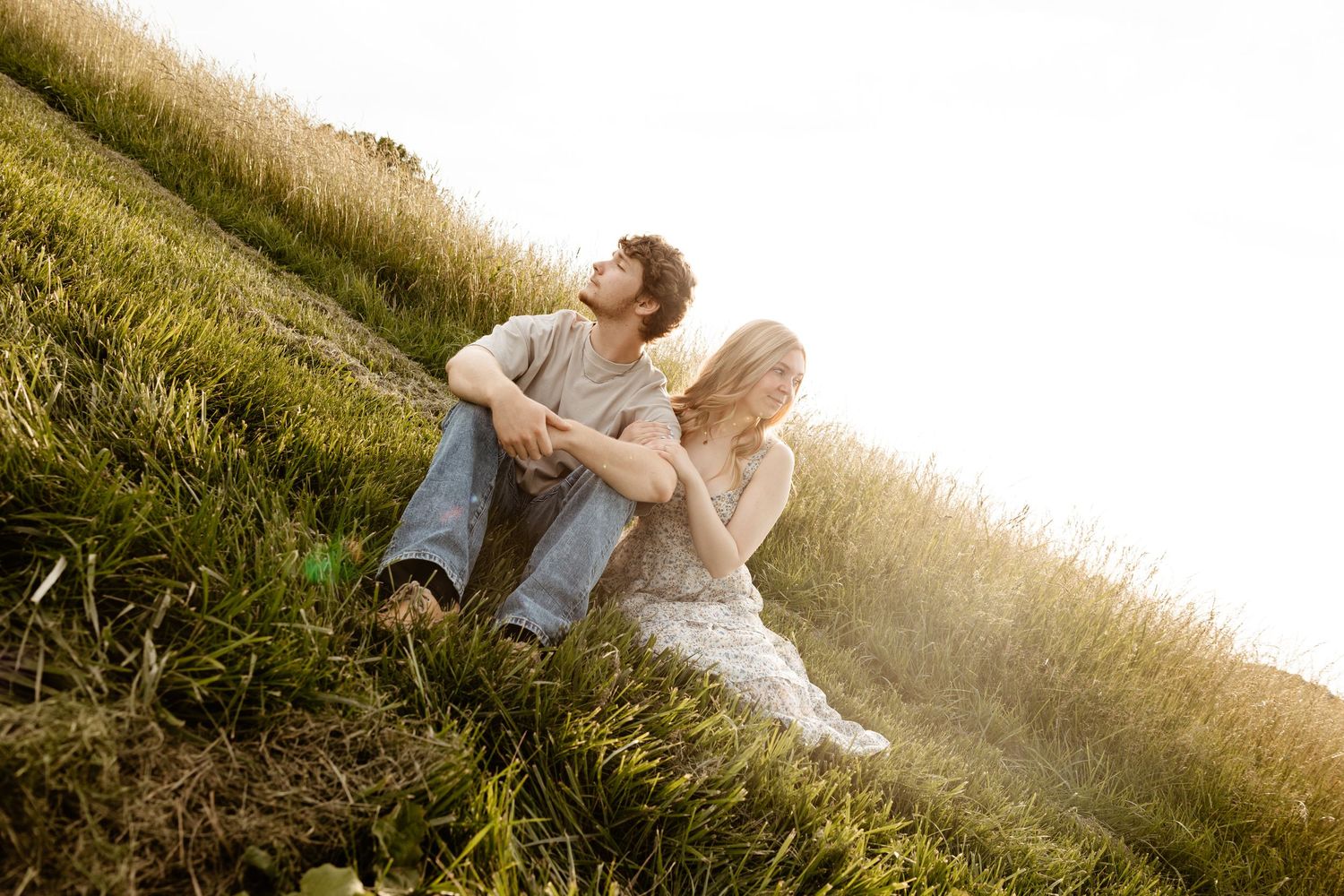 Young couple sitting together on a sunny hillside meadow enjoying a peaceful moment outdoors.