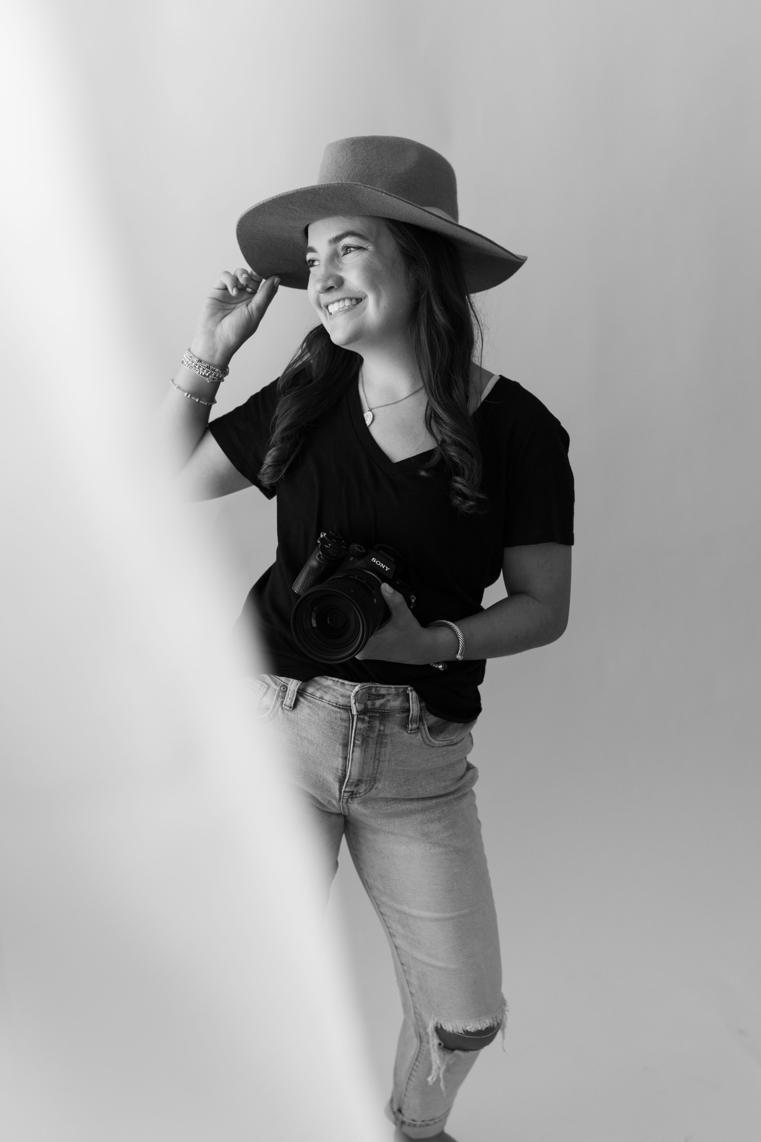 Artistic black and white portrait of woman in wide-brimmed hat and casual attire.