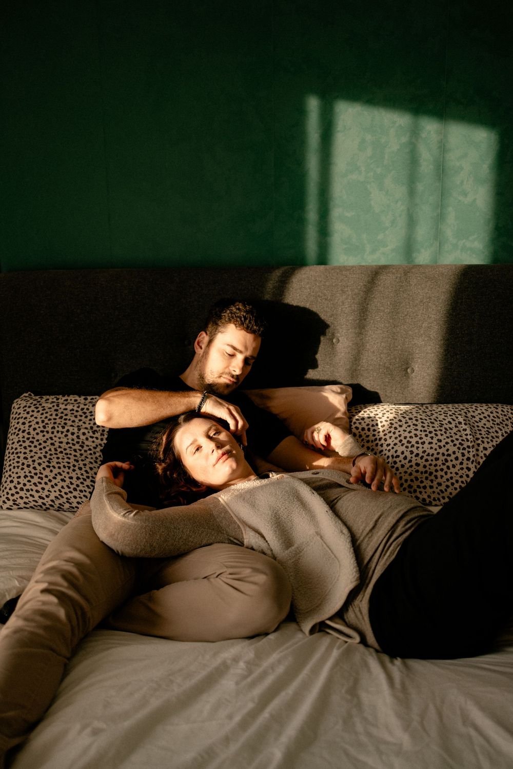 Person lying down on a patterned couch in dim lighting with sunlight streaming through nearby windows.