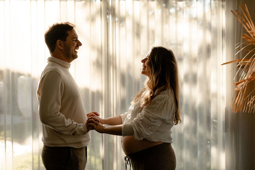 A couple shares an intimate dance together in a sunlit room with sheer curtains creating a romantic atmosphere.