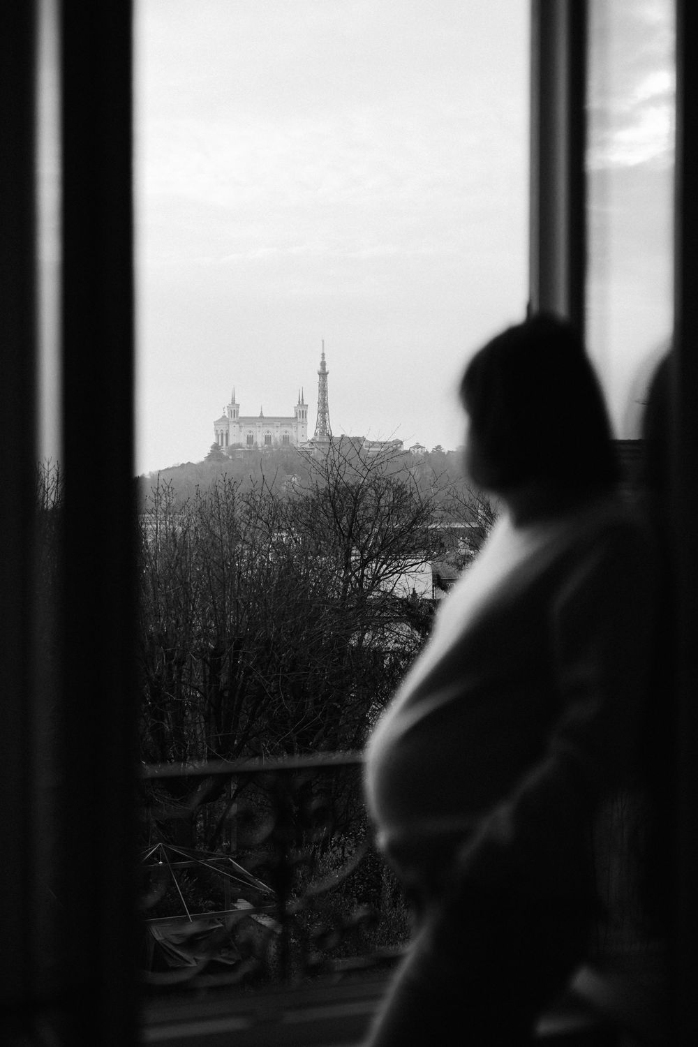 Silhouettes of people looking out through window bars at a distant castle on a misty hill.