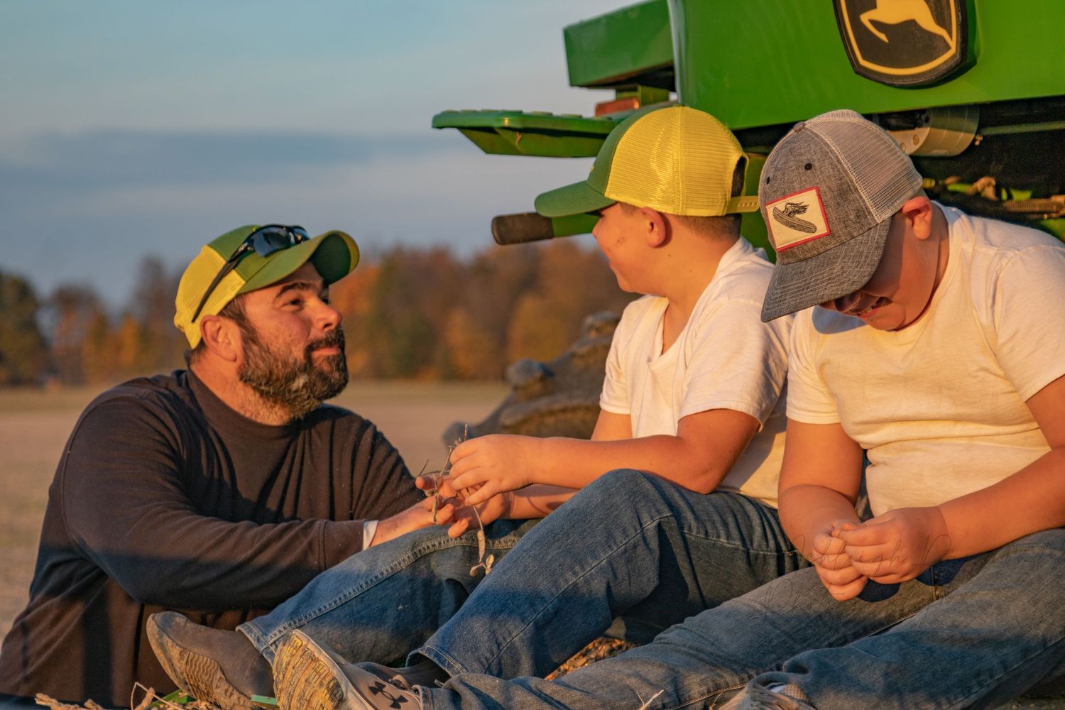A father and two boys sit on a tractor, enjoying a sunny fall day outdoors together.