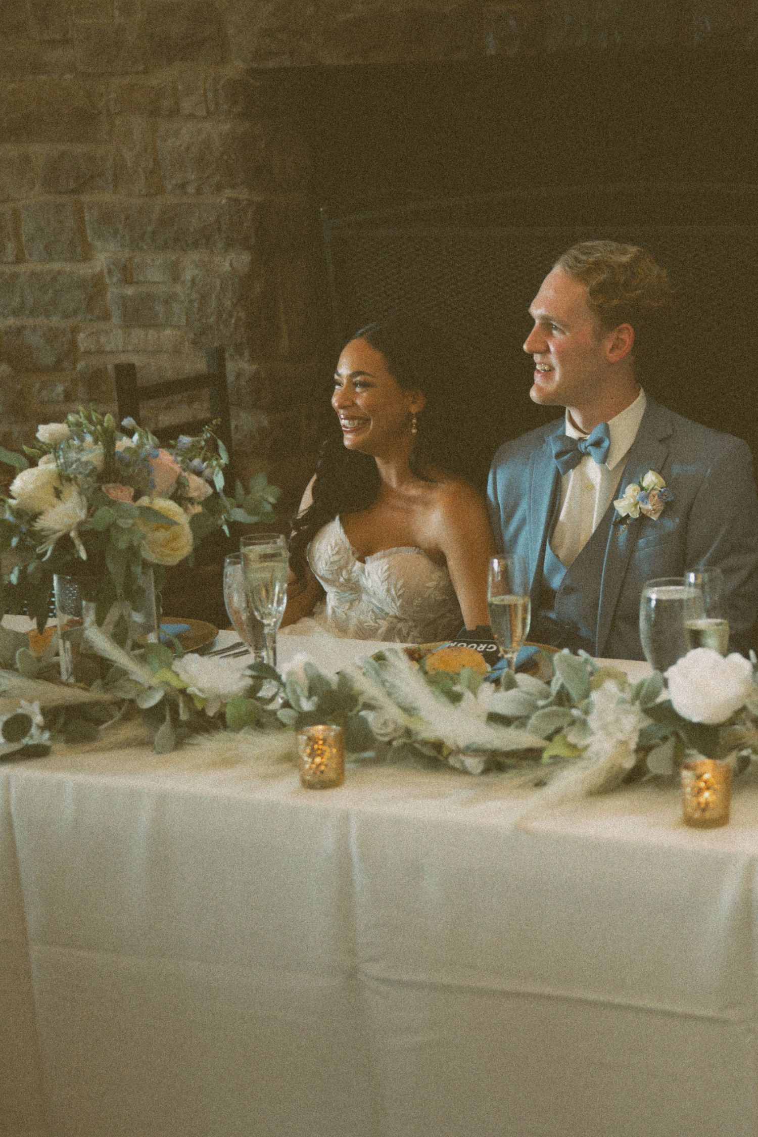 Newlyweds share a joyful moment at their reception table decorated with elegant floral arrangements.