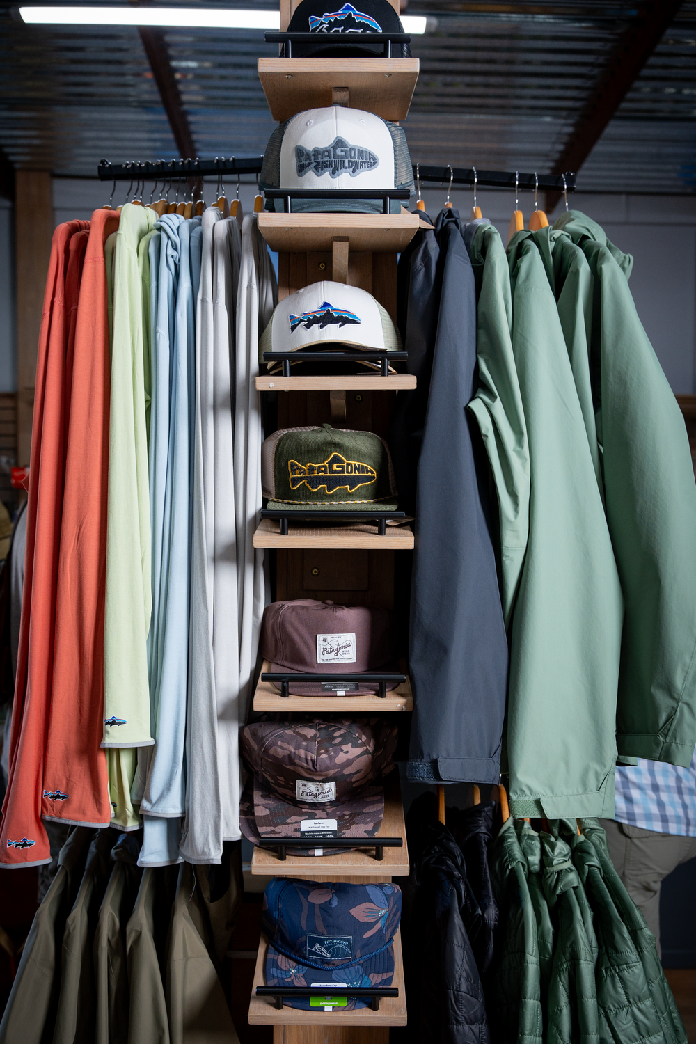 Retail display of outdoor apparel with fishing-themed hats and jackets on wooden shelving.