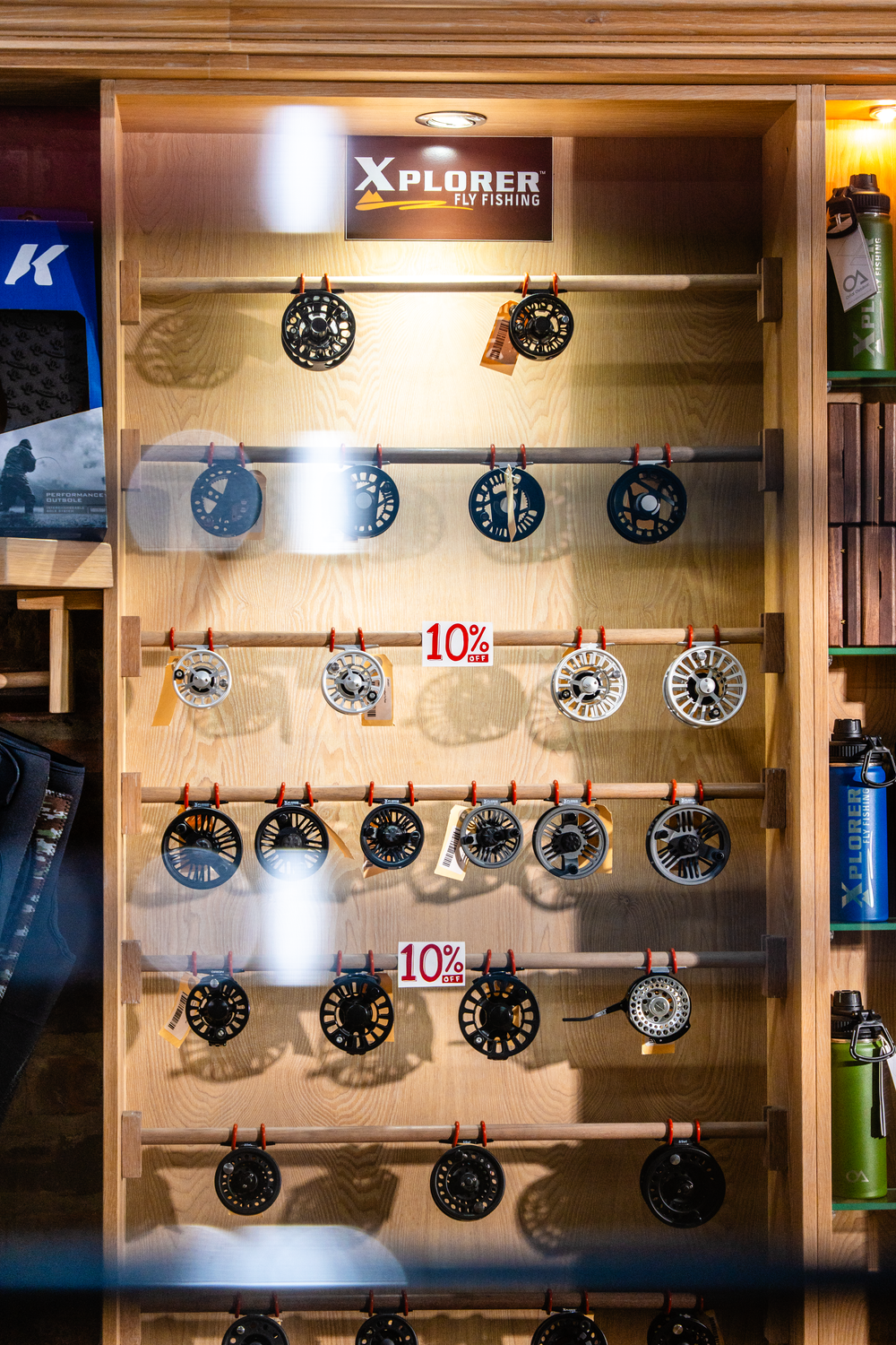 Wall display of fishing reels mounted on illuminated wooden panels.