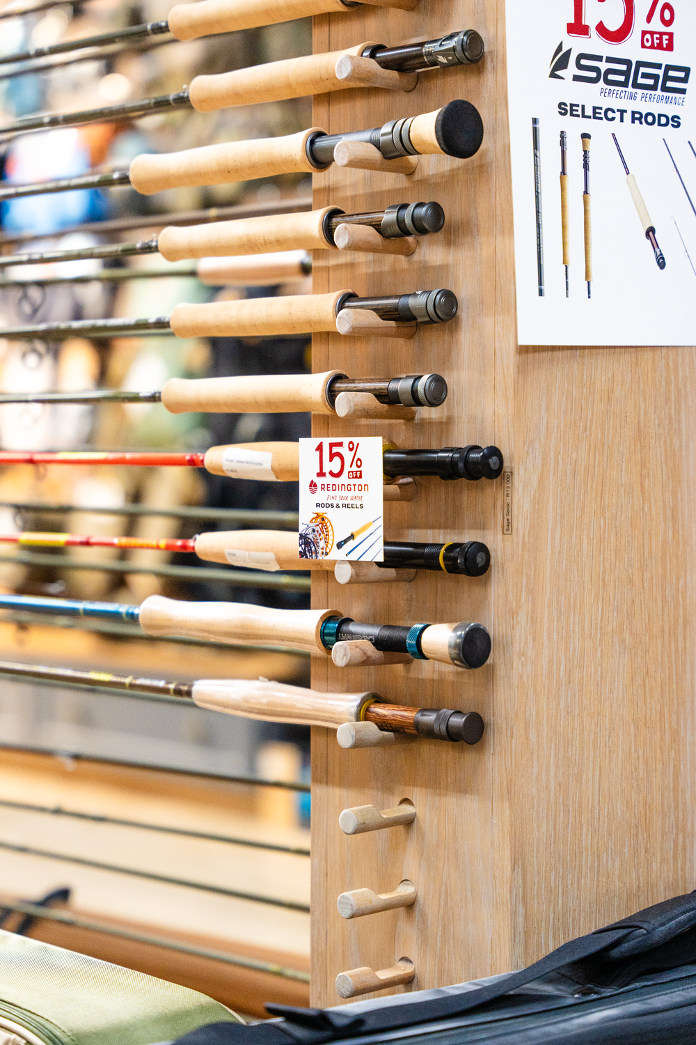 Multiple fishing rods mounted on a wooden display wall with a 15 percent off sale sign.