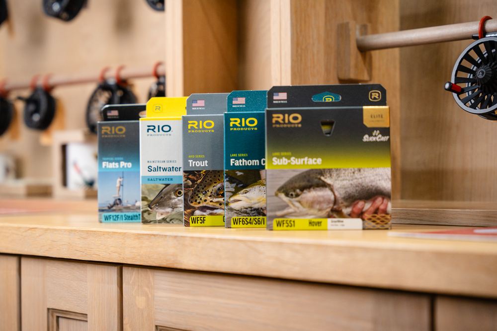 Collection of RIO fly fishing line boxes displayed on wooden shelf.
