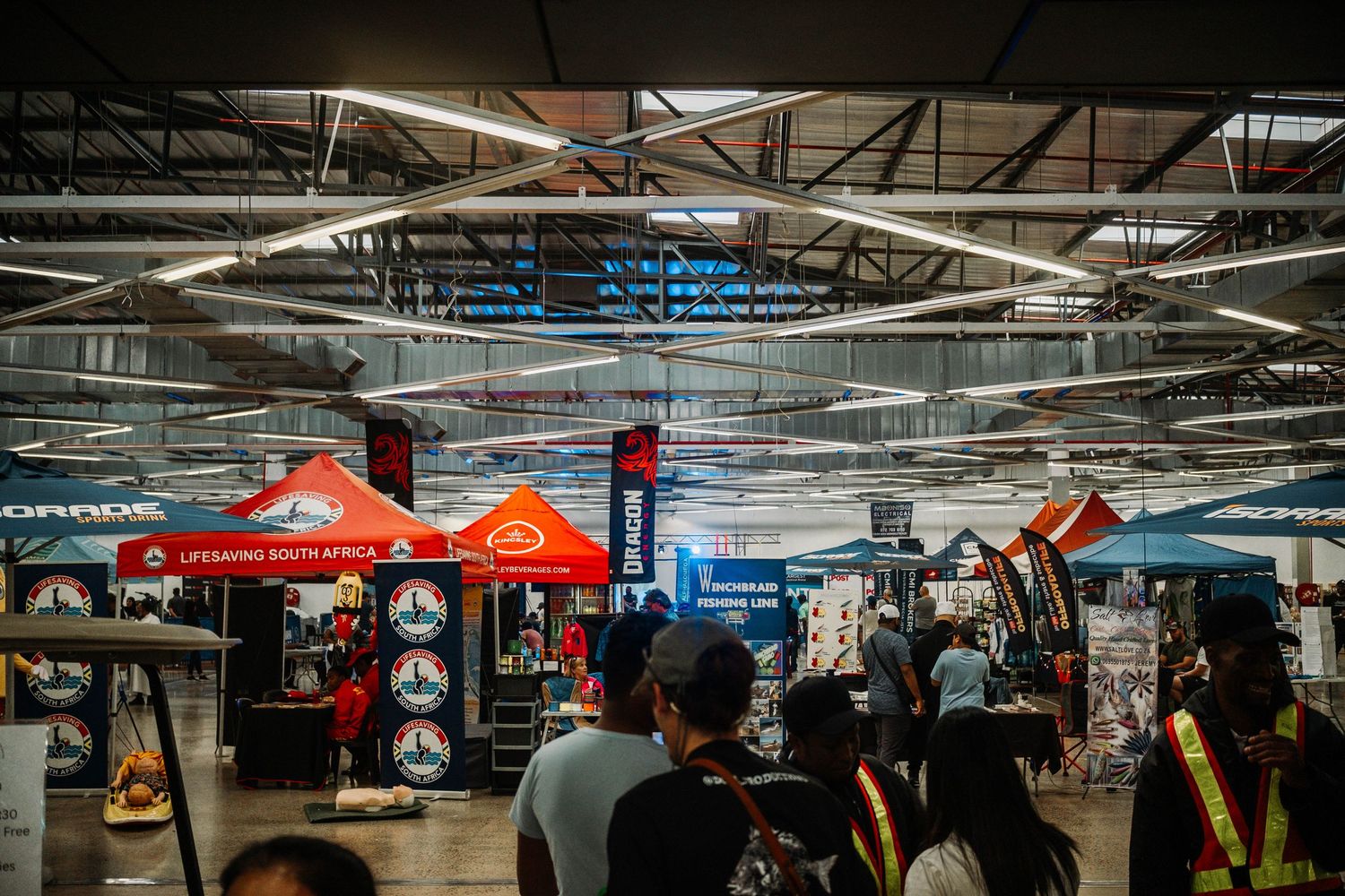 Large indoor marketplace with various vendor stalls and tents under bright industrial lighting.