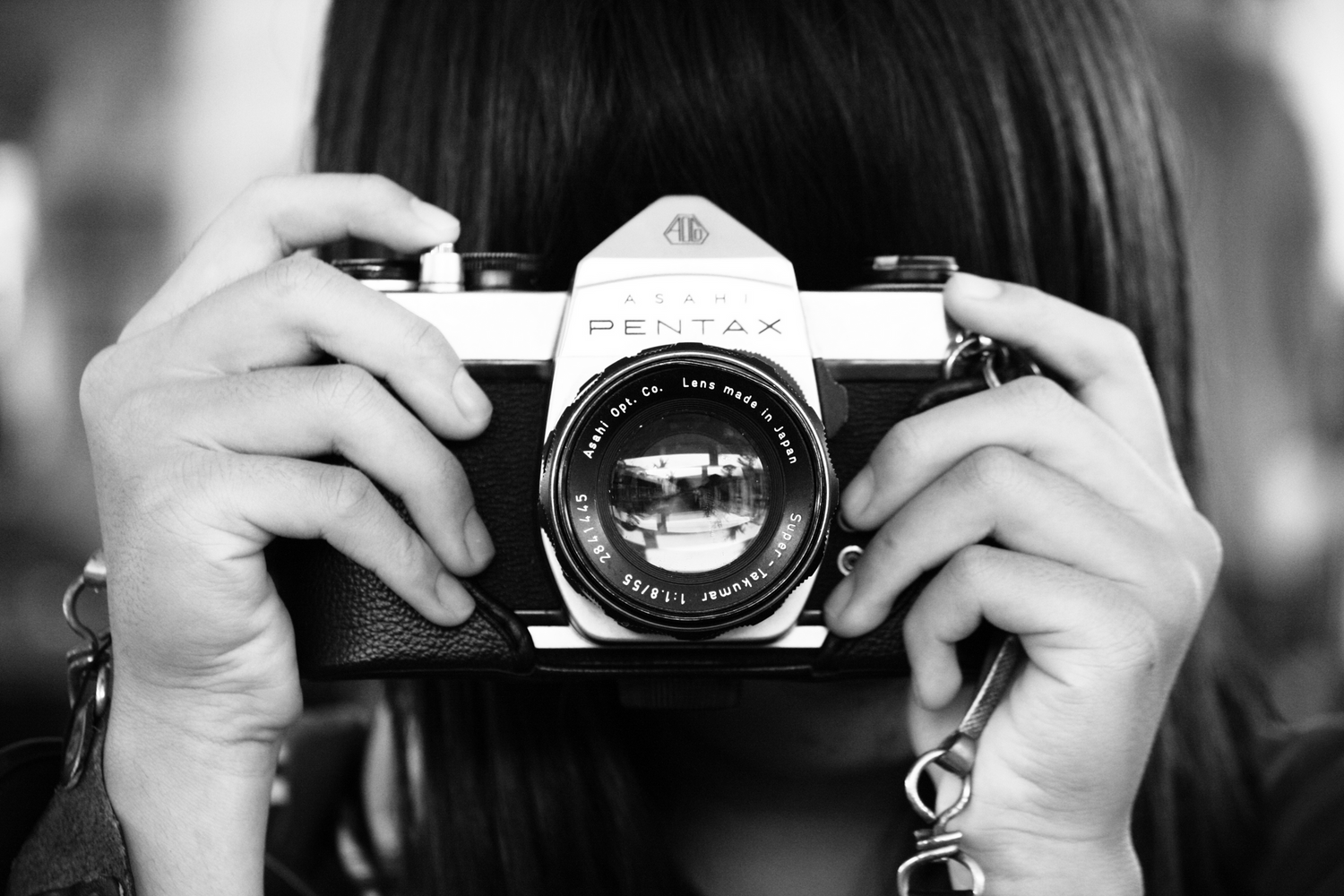 Black and white image of a girl holding a vintage camera in front of her face like she is taking a picture.